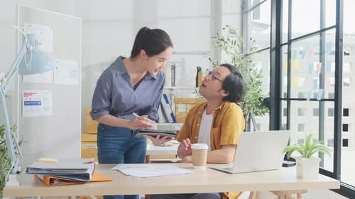 Two young Asian startup partners are working in a casual small business office.