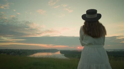 CloseUp of Woman in White Dress Gazing at Lake During Sunset in Serene Field