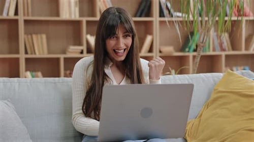 Excited Beautiful Caucasian Woman Sitting with Laptop and Raising Fist in Cheerful Gesture