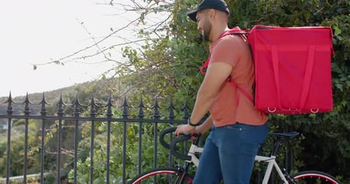 Courrier masculin démontant le vélo, le poussant contre une clôture en fer, appuyant sur l'interphone, livrant le colis