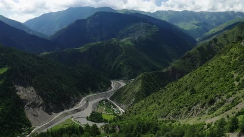 Aerial View of a Serpentine Road in Lush Green Mountains with a Small Village