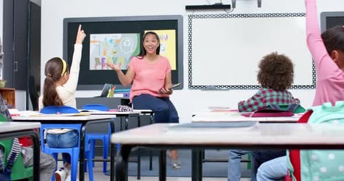 In school, teacher engaging with students raising hands in classroom discussion