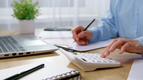 Close-up of a woman's hands using a calculator and writing on an office desk. Concept of financial