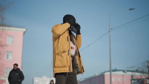 Photographer Aiming Vintage Camera on Snowy Street Under Bright Winter Sun