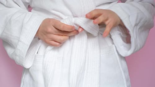 Jeune femme attachant une sangle sur son peignoir en gros plan sur fond rose.