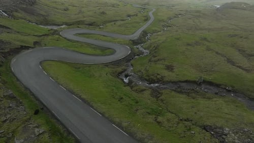 Scenic aerial shot flying over a curvy road through the green mountains of Faroe Islands, Denmark