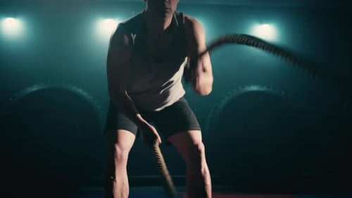 Man Exercises with Battle Ropes in Dark Gym