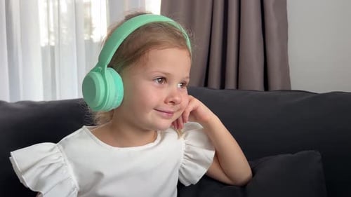 Little Girl Emotional Enjoying Music Using Green Kids Headphones in Home