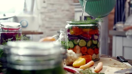 Pouring Brine into a Glass Jar of Layered Colorful Vegetables