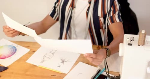 Biracial male fashion designer looking at sketched designs in studio, slow motion
