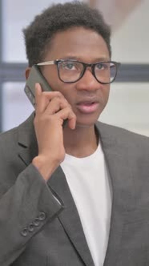 Young Man Talking on Phone Indoors Wearing Glasses