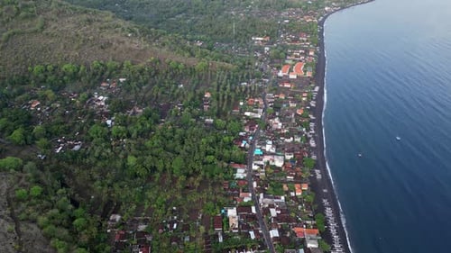 Drone top down view of a small village stretching out along the coast with black sand beaches and vo