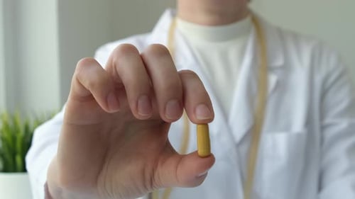 Close Up Female Doctor Holding Yellow Capsule in Hand in Clinic Office