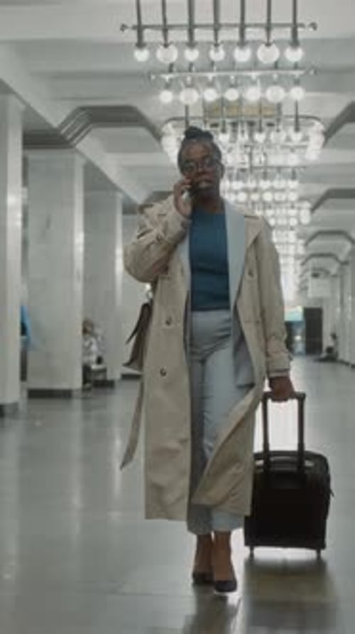 Vertical of Lady Talking on Phone While Walking in Subway with Suitcase