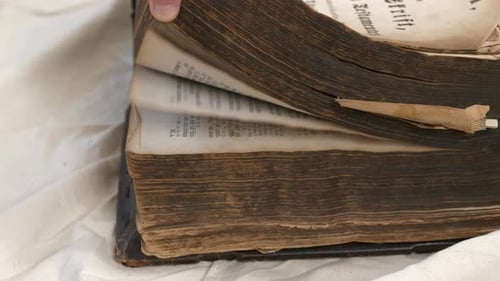Male hand flicks through pages of aged holy bible on table. Close up. Static shot.