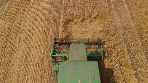 Aerial top down view green combine Harvester working on large wheat field