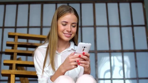 Woman In White Clothing Use Portable Gadget For Browsing Social Networks. Model Sitting On The St...