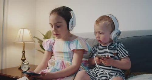 Siblings Using Smartphones With Headphones on Couch