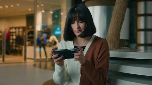 Woman Lady Female Gamer Girl Indoors in Shopping Mall Sitting Playing with Mobile Phone in Video