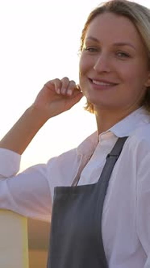 Une femme souriante portant un tablier au coucher du soleil rayonnant de joie et de contentement dans la lumière chaude de la nature