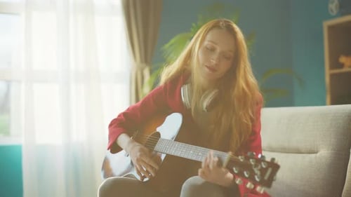 Young Woman Plays Guitar on Couch at Home