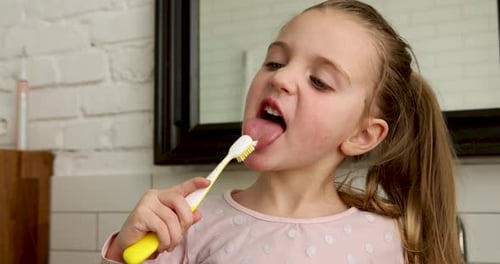 Niña cepillándose la lengua con el cepillo de dientes en el baño por la mañana