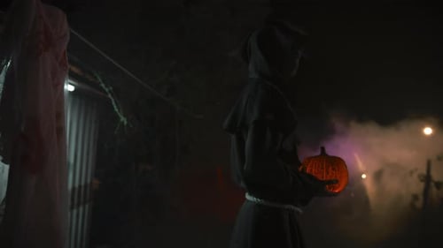 Grim Figure Holding Glowing Jack-o'-Lantern at Night