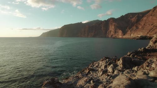 A man and woman stand together on the rocks at Los Gigantes Cliffs in Tenerife, with the ocean and c