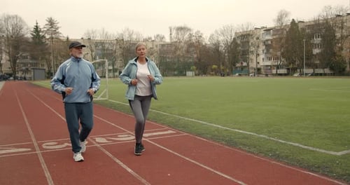 Mature Runners Couple Athletes Jogging Together in the Morning in Stadium Park