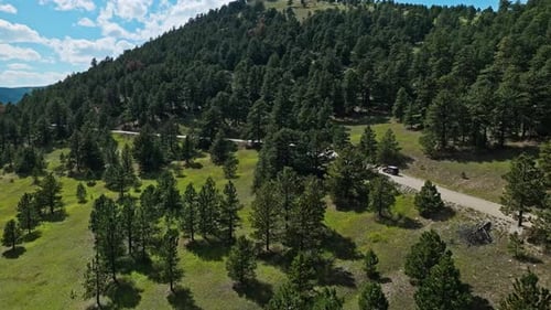 Drone orbits tracking car driving along rugged winding mountain offroad path