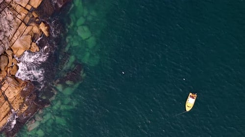 aerial top-down view of a small white boat floating in turquoise coastal waters near a rocky