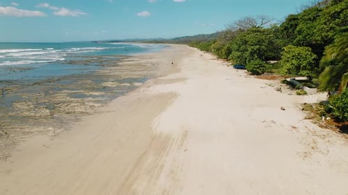 Long sandy beach stretching along coast with lush green trees in Costa Rica