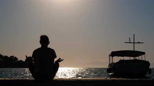 The female sits on the pier in the lotus position.