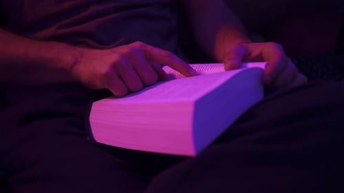 Close-up shot of a man reading a book under a vibrant light