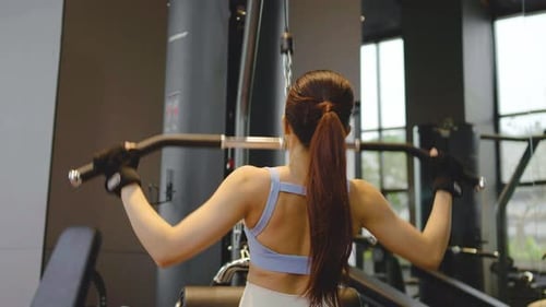 Rear view of Young asian woman fitness exercises at gym lat pulldown machine