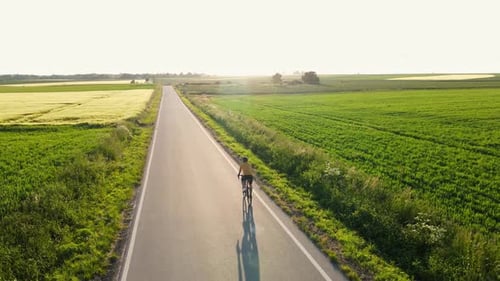 Cyclist Riding Bicycle on Countryside Road Near Agricultural Fields