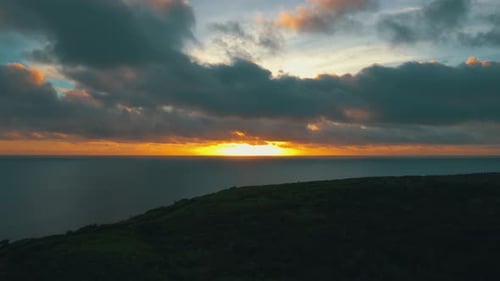 fliegen Sie während eines bewölkten Sonnenuntergangs vom Meer über einem Waldufer einer Insel rückwärts.