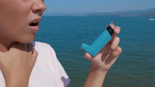 Teenager Uses Asthma Inhaler by Ocean on Sunny Day