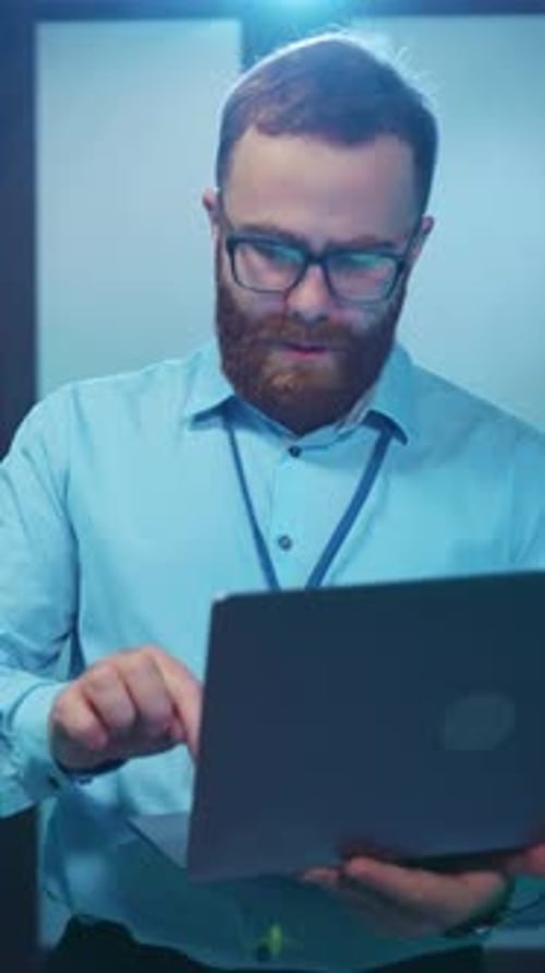 An IT Specialist Focused on Working on a Laptop Inside a Modern and Efficient Data Center