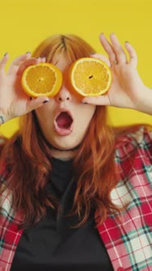 Playful Redhaired Woman Covering Eyes with Orange Slices