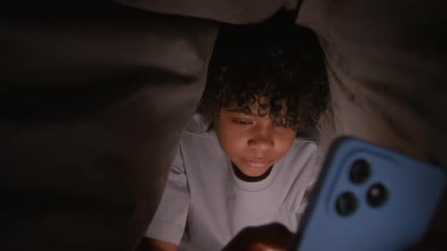 Child Using Cell Phone Under Blanket at Night