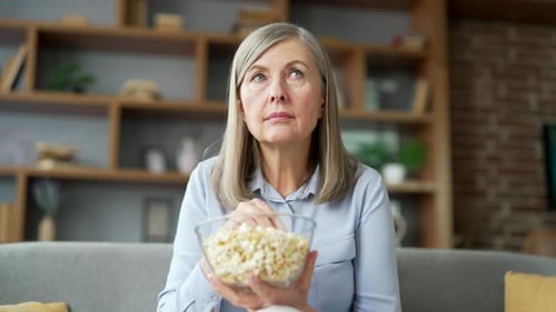 Woman Eating Popcorn While Watching Television at Home