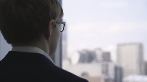 Businessman Looking Out Office Window at City Skyline
