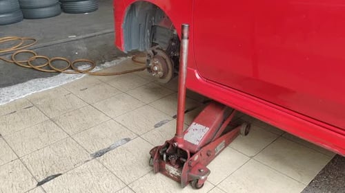 A small red car is seen in a workshop, undergoing a tire change.