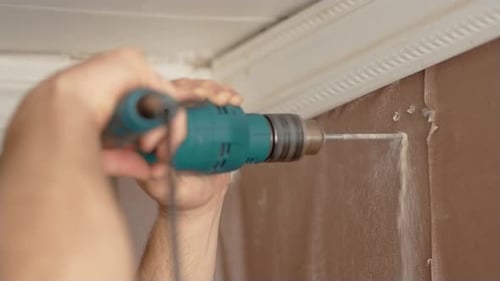 Economical Renovation in Old Apartment Man Drills Wall with Hammer Drill in His Home Close Up