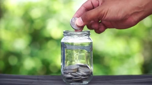 Hand Adding Coins to Jar for Savings