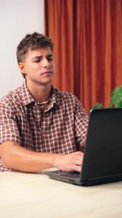 Frustrated Young Man Struggling with Issues While Sitting at a Desk in Front of an Open Laptop