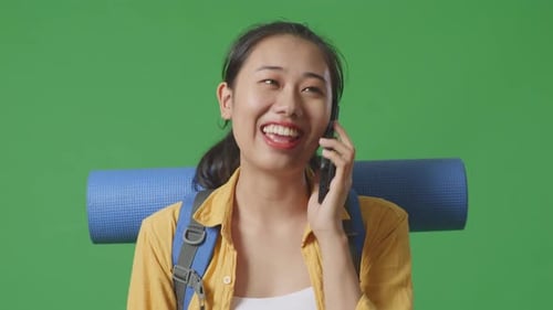 Close Up Of Asian Female Hiker Smiling And Talking On Smartphone While Standing On Green Screen