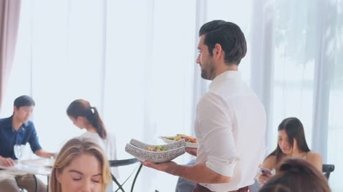 Caucasian young waiter serving foods to female customer in restaurant.