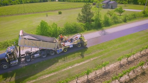 A country road being paved by a construction crew with an asphalt truck